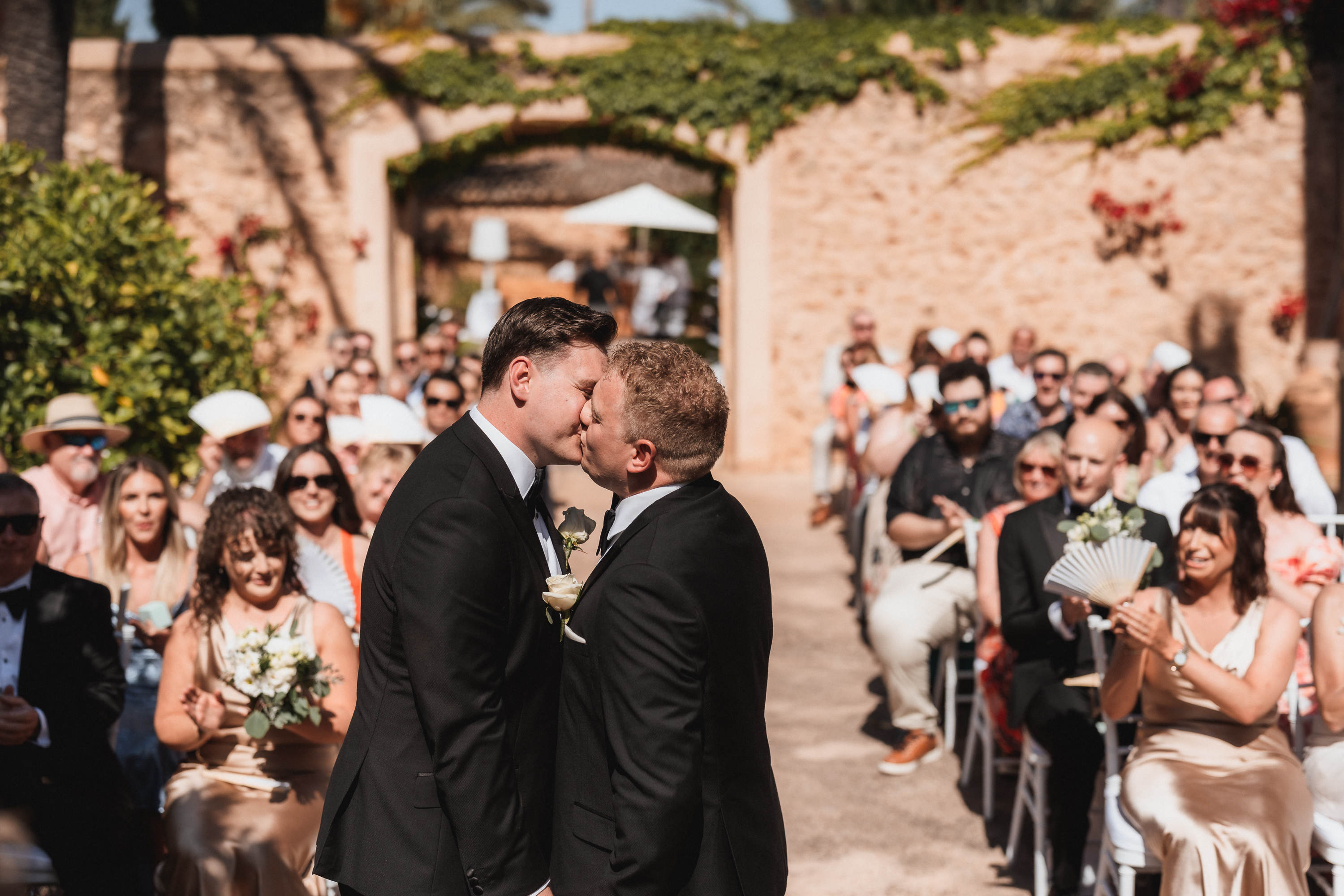 First kiss of two grooms during wedding ceremony at Finca Son Mir Mallorca with guests celebrating, photographed by Photos by Ville