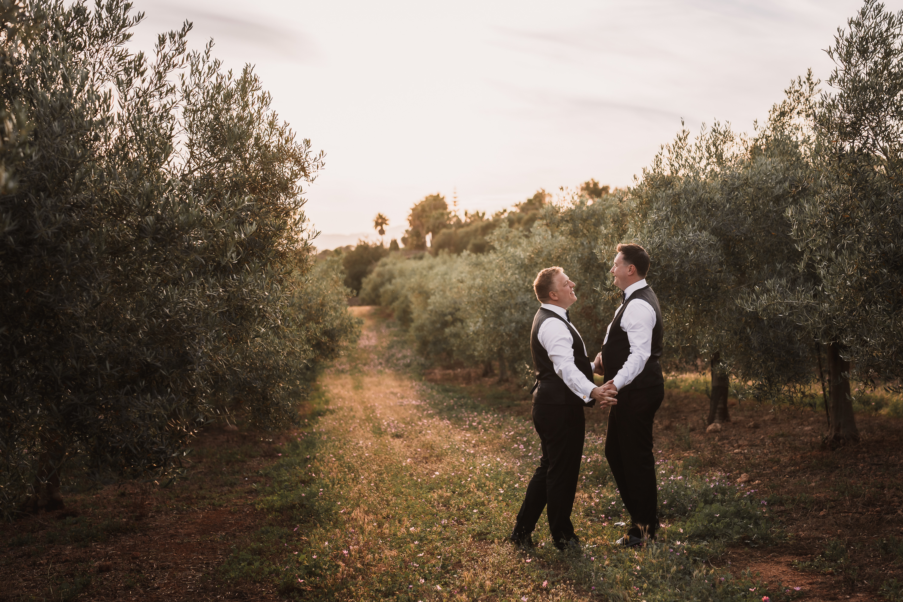 Two grooms holding hands at sunset between olive trees in Mallorca photographed by Photos by Ville