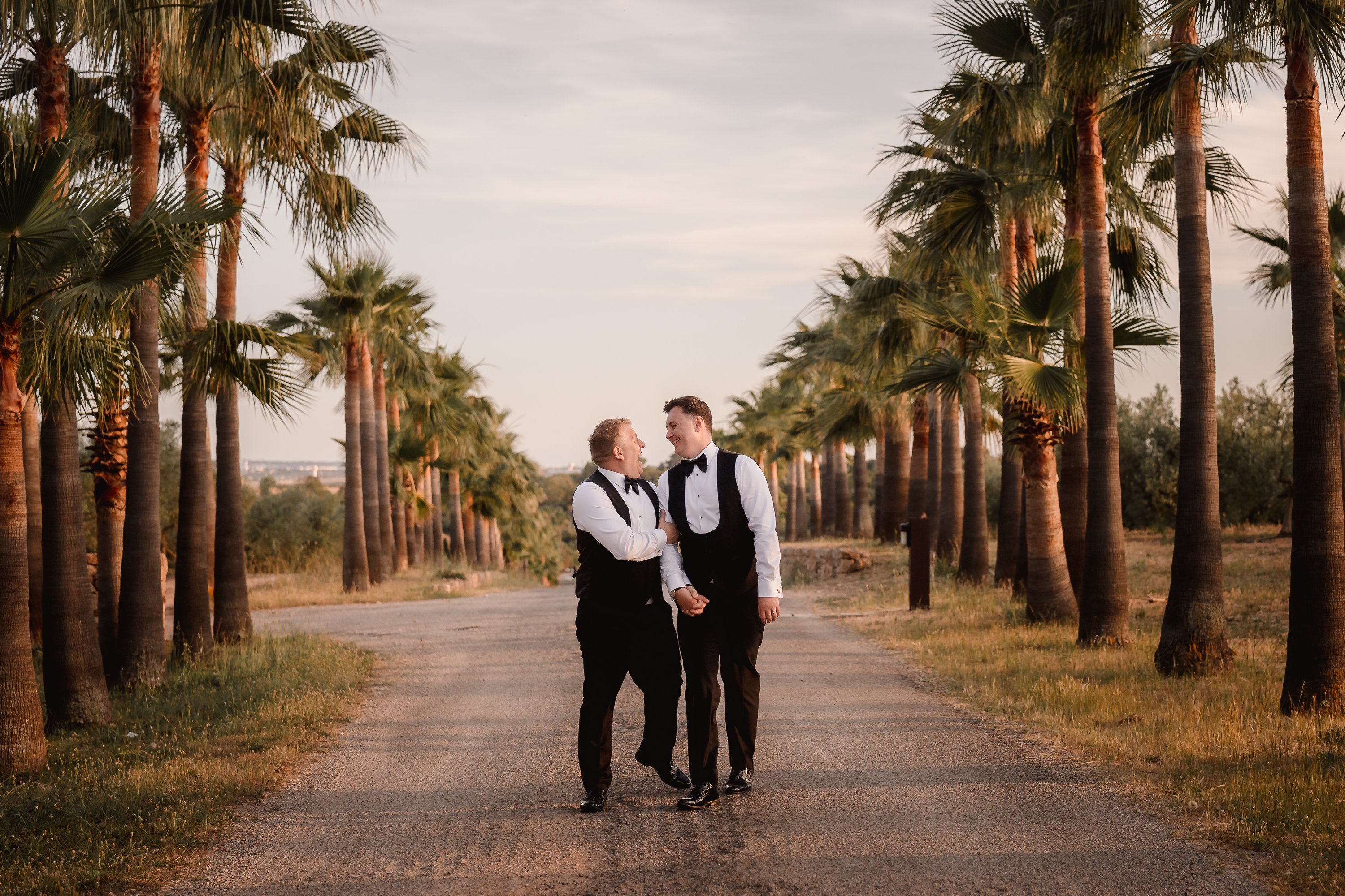Two grooms walking between palm trees having fun during wedding photoshoot in Mallorca